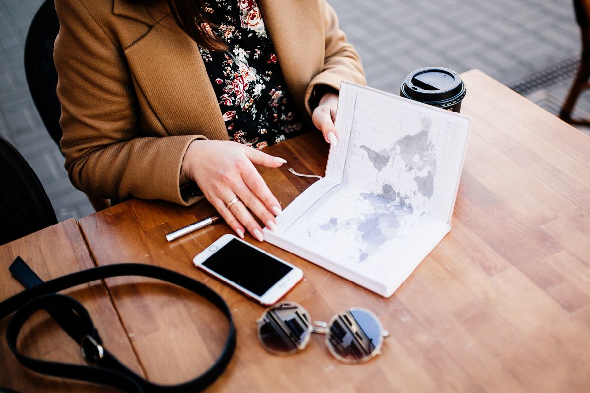 Personne préparant un voyage sur une table en bois avec une carte, un carnet et un smartphone
